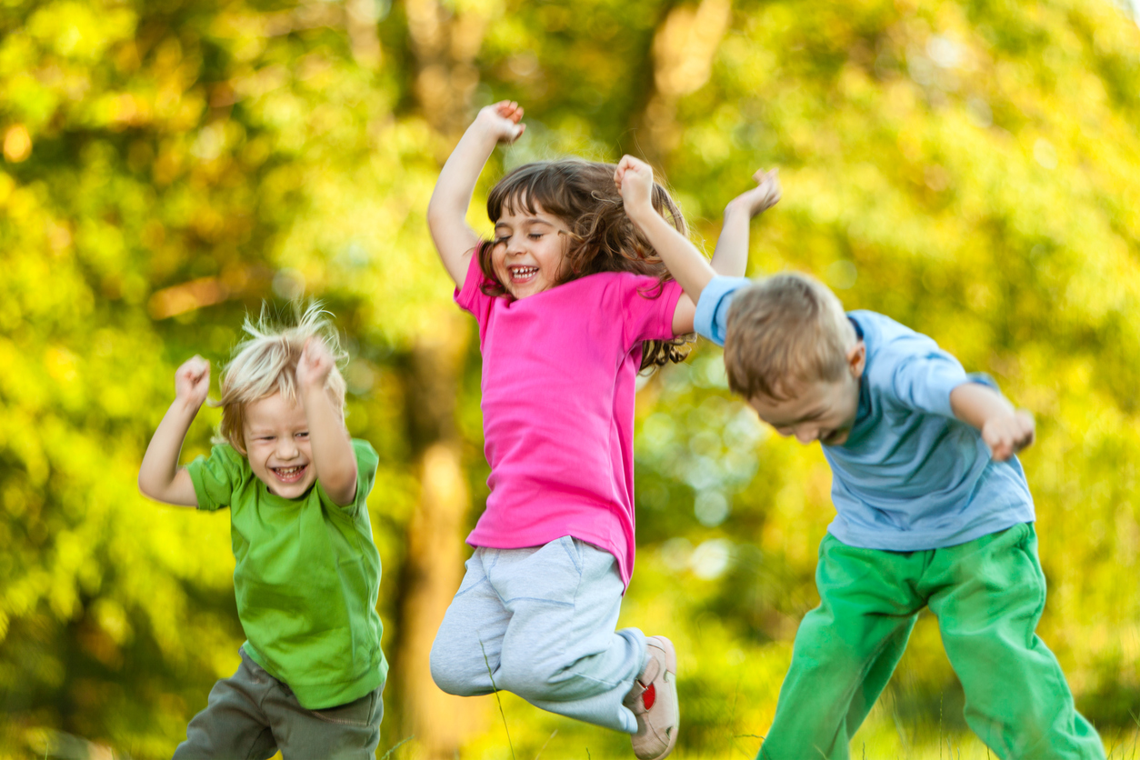 Group Of Three Happy Children Jumping Outdoors